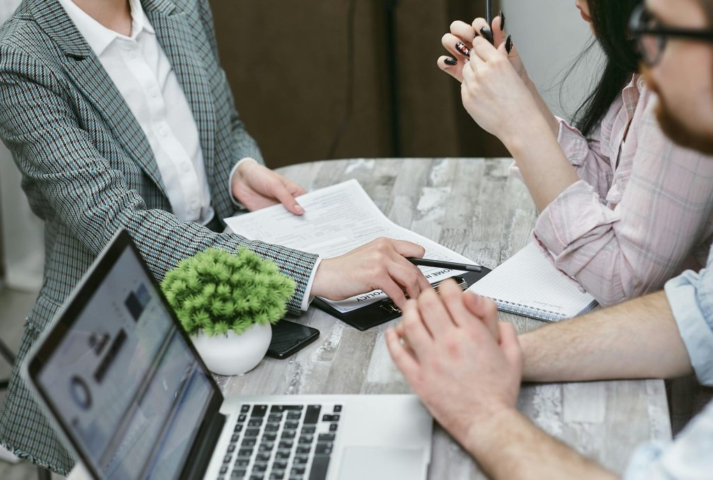Réunion professionnelle discutant d'accords commerciaux avec des ordinateurs portables et des documents sur une table rustique.