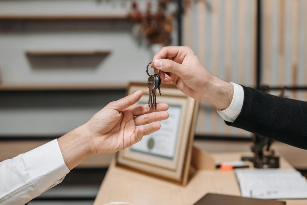 Vue détaillée des mains échangeant des clés dans un environnement de bureau professionnel, symbolisant des transactions immobilières ou commerciales.