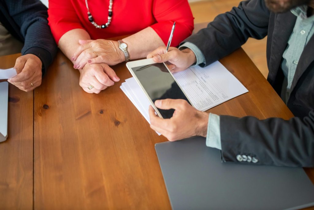Réunion d'affaires autour d'une table en bois avec un consultant examinant des documents et utilisant une tablette numérique.