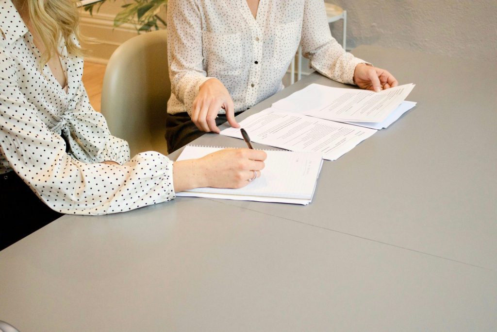 Une femme signant sur du papier blanc à côté d'une femme